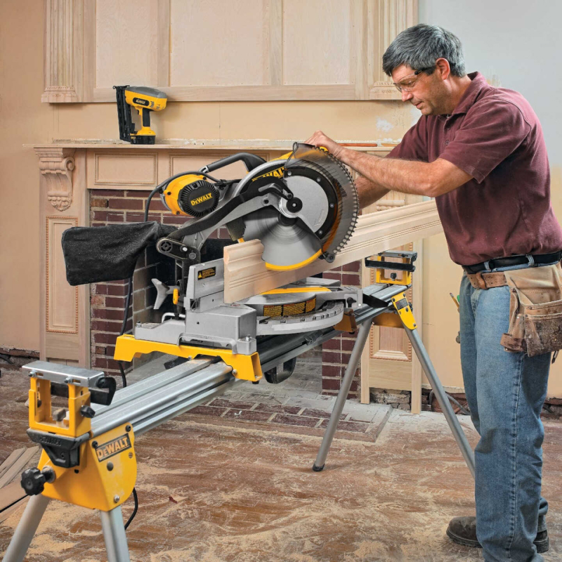 man standing and using a large miter saw to cut a piece of trim